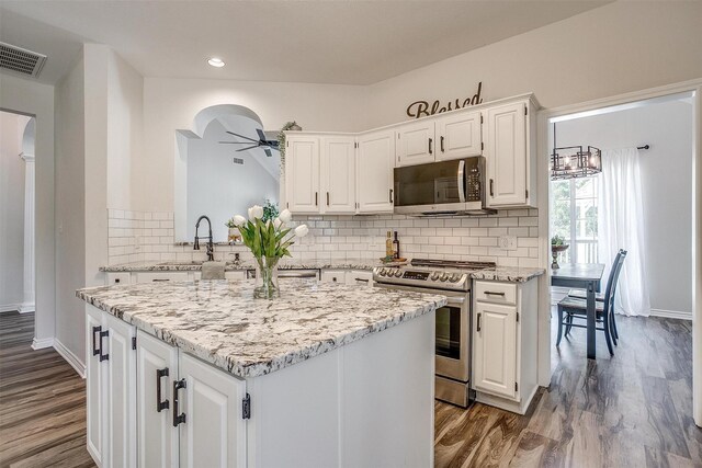 kitchen with light stone counters, stainless steel appliances, ceiling fan, wood-type flooring, and white cabinetry