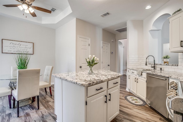 kitchen featuring white cabinets, light hardwood / wood-style flooring, a kitchen island, and stainless steel dishwasher