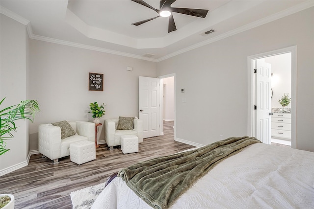 bedroom featuring hardwood / wood-style floors, connected bathroom, a tray ceiling, and ceiling fan