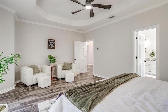 bedroom with wood-type flooring, ensuite bath, ceiling fan, crown molding, and a tray ceiling