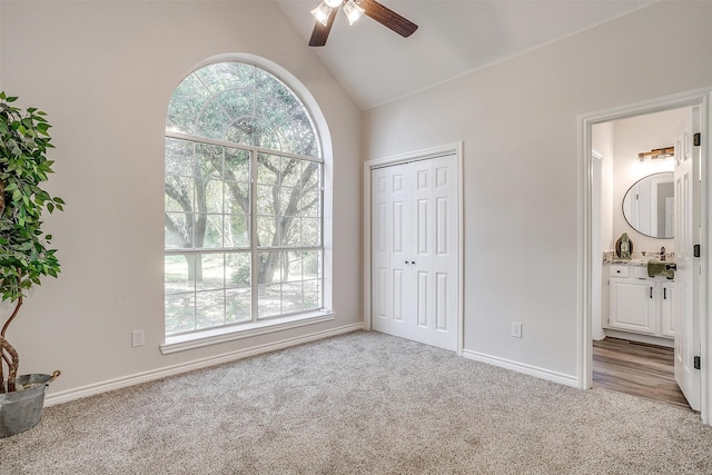 unfurnished bedroom with connected bathroom, ceiling fan, light colored carpet, and lofted ceiling