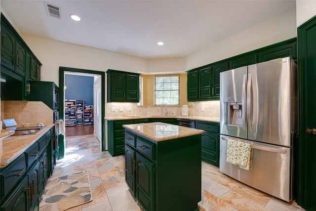 kitchen featuring stainless steel fridge, tasteful backsplash, light stone counters, sink, and a kitchen island