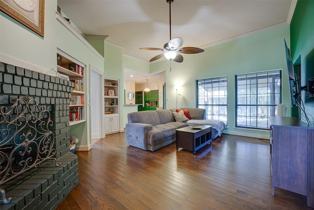 living room featuring ceiling fan, a brick fireplace, dark hardwood / wood-style flooring, built in features, and crown molding