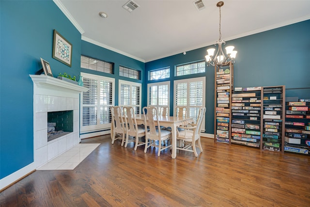 dining space with a tile fireplace, a baseboard radiator, an inviting chandelier, wood-type flooring, and ornamental molding