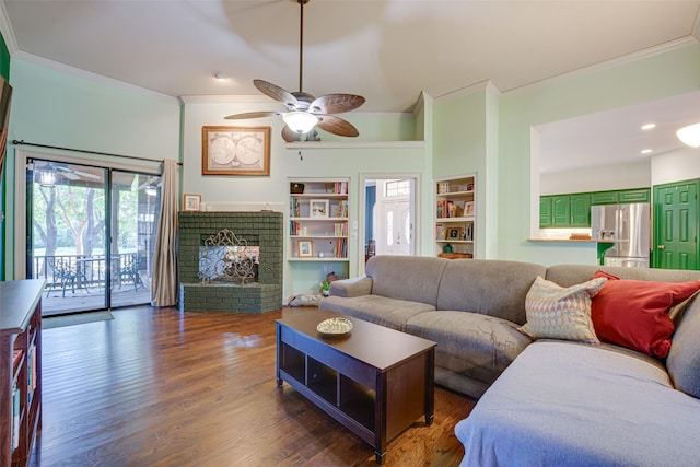 living room with dark hardwood / wood-style flooring, ceiling fan, crown molding, built in features, and a fireplace