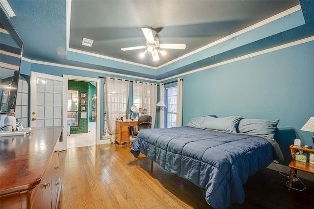 bedroom with ornamental molding, light hardwood / wood-style floors, ceiling fan, and a tray ceiling