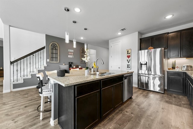 kitchen with appliances with stainless steel finishes, pendant lighting, sink, light stone counters, and a center island with sink