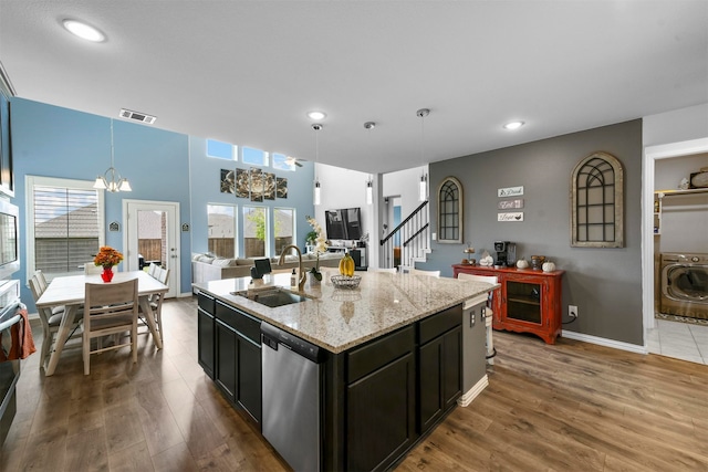 kitchen with stainless steel appliances, hardwood / wood-style floors, sink, an island with sink, and washer / dryer