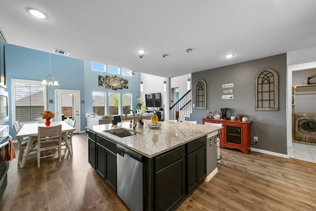 kitchen with pendant lighting, sink, stainless steel appliances, a center island with sink, and washer / clothes dryer