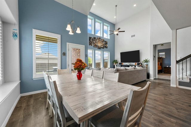 dining room with ceiling fan with notable chandelier, dark wood-type flooring, and a high ceiling