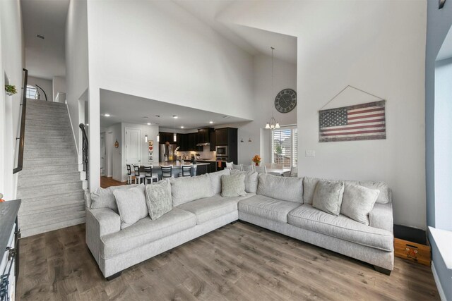 living room featuring a towering ceiling, a chandelier, and wood-type flooring