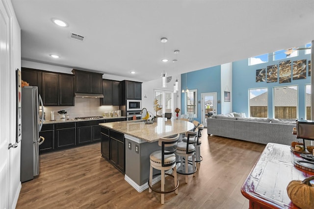 kitchen featuring pendant lighting, appliances with stainless steel finishes, dark hardwood / wood-style floors, tasteful backsplash, and a center island with sink