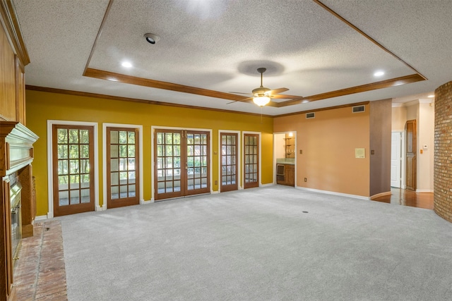 unfurnished living room with a raised ceiling, a brick fireplace, light colored carpet, and a textured ceiling