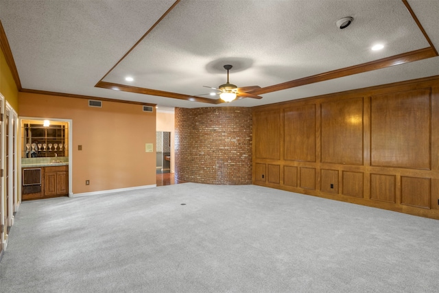 interior space featuring ceiling fan, a tray ceiling, light colored carpet, ornamental molding, and a textured ceiling