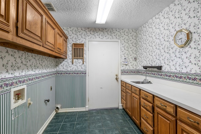 laundry room with a textured ceiling, dark tile patterned flooring, sink, and cabinets