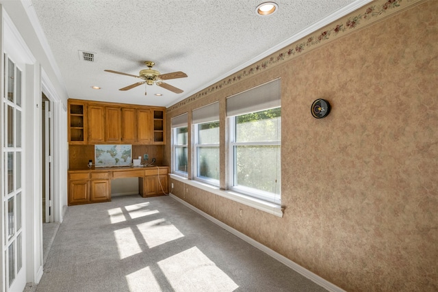 kitchen with ceiling fan, crown molding, light colored carpet, built in desk, and a textured ceiling