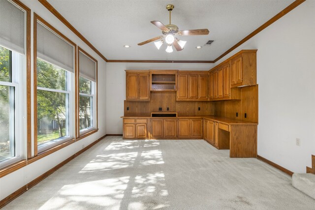 kitchen with ceiling fan, built in desk, ornamental molding, and a healthy amount of sunlight