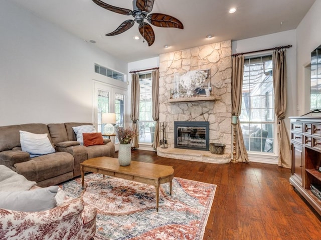 living room featuring a healthy amount of sunlight, a stone fireplace, dark wood-type flooring, and ceiling fan