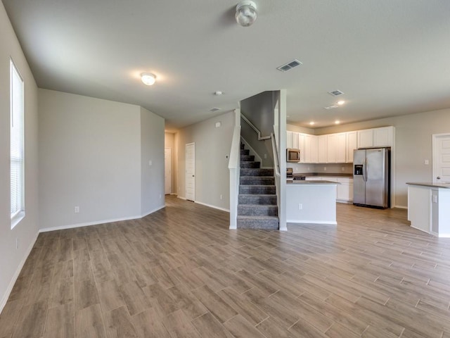 unfurnished living room featuring baseboards, visible vents, light wood finished floors, and stairs