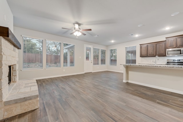 unfurnished living room featuring ceiling fan, sink, dark wood-type flooring, and a stone fireplace