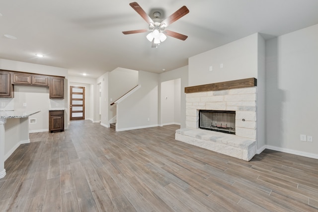 unfurnished living room with wood-type flooring, ceiling fan, and a stone fireplace