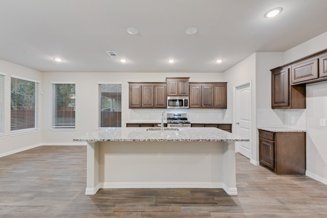 kitchen with appliances with stainless steel finishes, sink, an island with sink, and light stone counters