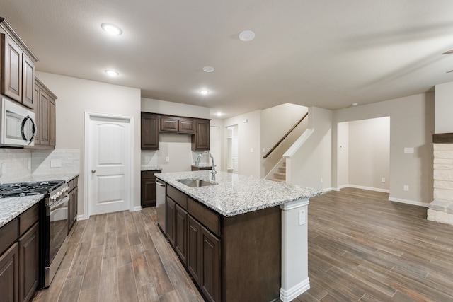 kitchen with sink, dark brown cabinets, a kitchen island with sink, appliances with stainless steel finishes, and hardwood / wood-style floors