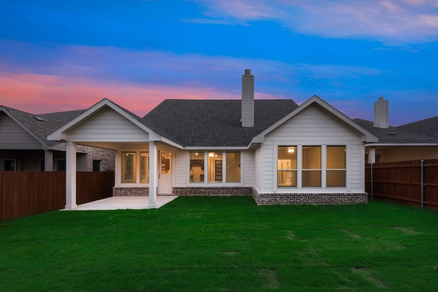 back house at dusk featuring a lawn and a patio area