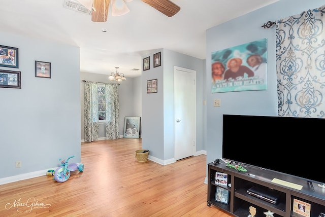 living room featuring ceiling fan with notable chandelier and light wood-type flooring