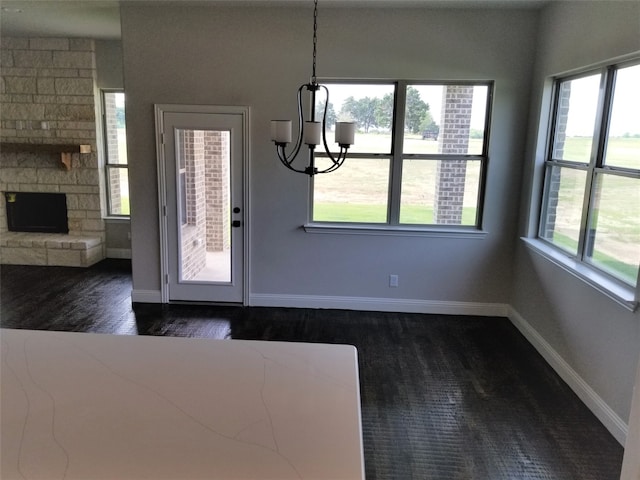 unfurnished dining area with a stone fireplace, dark wood-type flooring, a healthy amount of sunlight, and an inviting chandelier