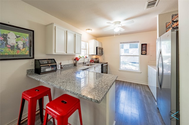 kitchen featuring white cabinetry, hardwood / wood-style flooring, light stone counters, ceiling fan, and stainless steel appliances