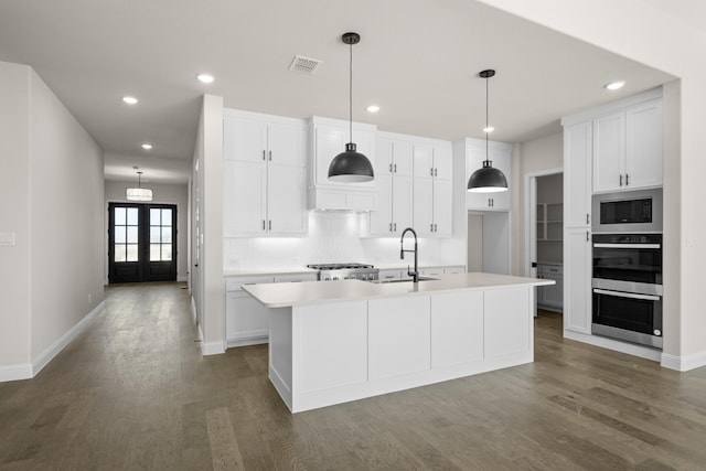 kitchen featuring an island with sink, french doors, built in microwave, white cabinets, and sink