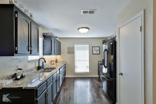 kitchen featuring dark hardwood / wood-style flooring, black refrigerator, sink, and light stone countertops