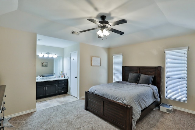 bedroom with multiple windows, light colored carpet, connected bathroom, and ceiling fan