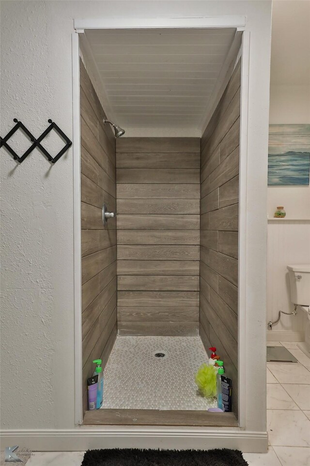 bathroom with toilet, a tile shower, and tile patterned flooring