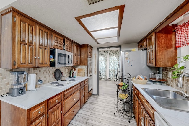 kitchen with light hardwood / wood-style floors, decorative backsplash, sink, appliances with stainless steel finishes, and a textured ceiling