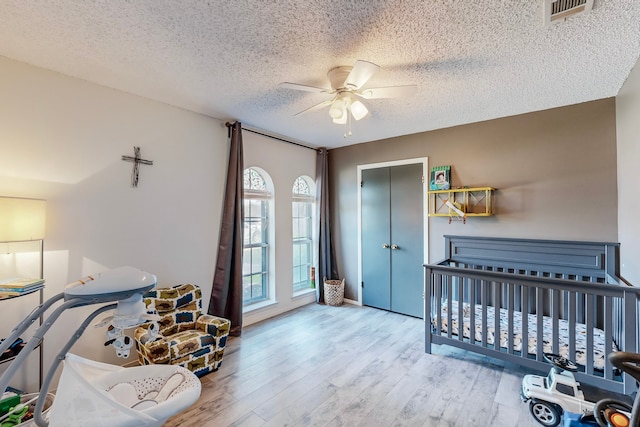 bedroom featuring a textured ceiling, ceiling fan, a nursery area, and light wood-type flooring