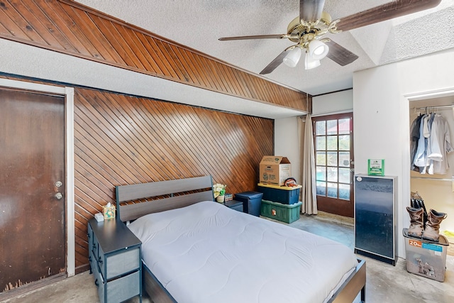 bedroom featuring ceiling fan, a textured ceiling, a closet, and wooden walls