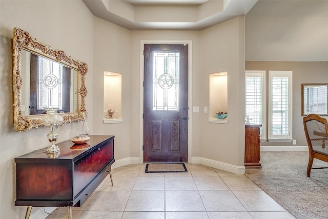 foyer with a tray ceiling, a healthy amount of sunlight, and light tile patterned floors