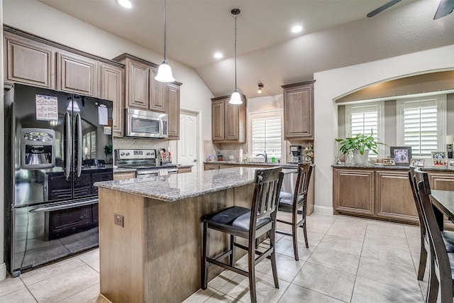 kitchen featuring a center island, stone counters, tasteful backsplash, light tile patterned floors, and stainless steel appliances