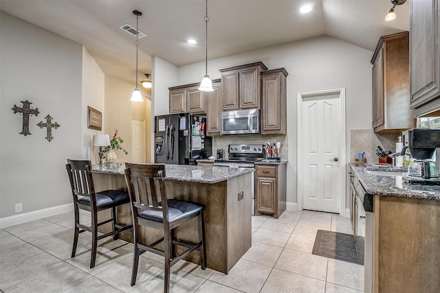 kitchen featuring light tile patterned flooring, dark stone counters, appliances with stainless steel finishes, tasteful backsplash, and lofted ceiling