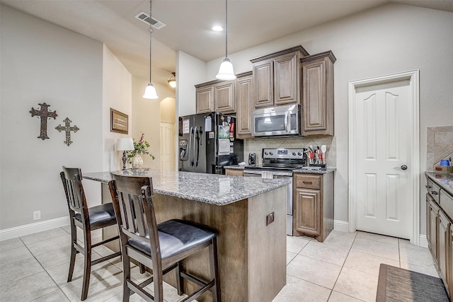 kitchen featuring a kitchen bar, tasteful backsplash, light tile patterned floors, stainless steel appliances, and pendant lighting