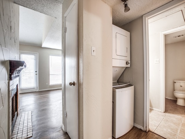 laundry area featuring a textured ceiling, light hardwood / wood-style flooring, and stacked washing maching and dryer