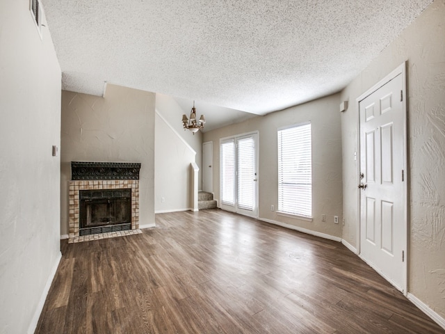 unfurnished living room with a fireplace, a textured ceiling, an inviting chandelier, and wood-type flooring