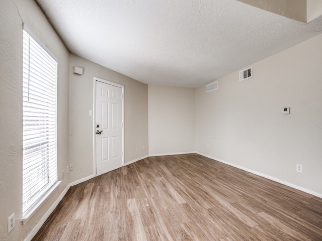 unfurnished room featuring plenty of natural light, a textured ceiling, and hardwood / wood-style floors