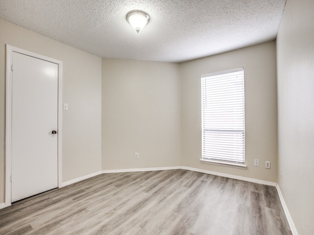 spare room featuring a textured ceiling, light hardwood / wood-style flooring, and a healthy amount of sunlight