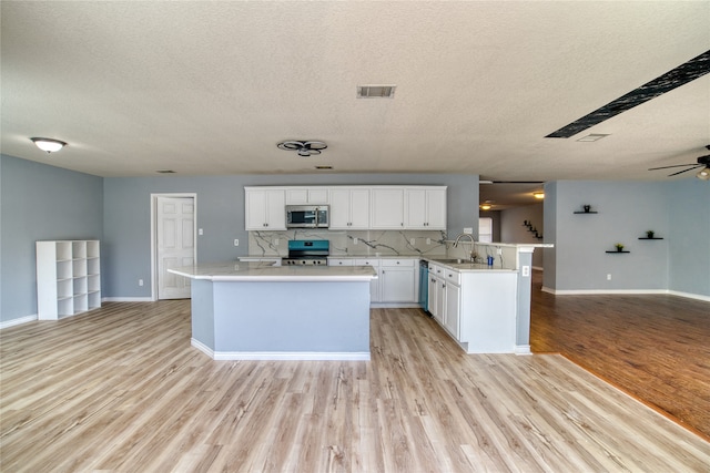 kitchen featuring appliances with stainless steel finishes, white cabinetry, light wood-type flooring, a kitchen island, and ceiling fan