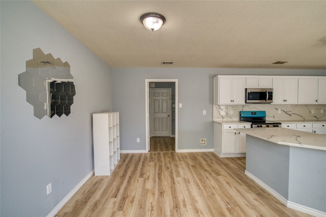 kitchen featuring white cabinets, decorative backsplash, appliances with stainless steel finishes, and light hardwood / wood-style floors