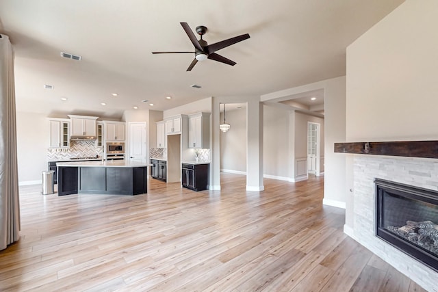 kitchen featuring ceiling fan, light hardwood / wood-style floors, an island with sink, and a fireplace