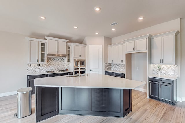 kitchen with appliances with stainless steel finishes, a kitchen island with sink, light hardwood / wood-style floors, tasteful backsplash, and white cabinets